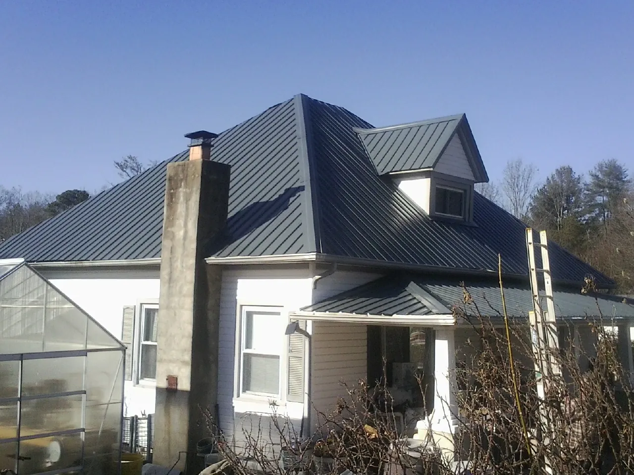 Dark blue standing seam metal roof on a white farmhouse with dormer — Slate & Tile Roof Repair by Roofing Brothers in Garnett