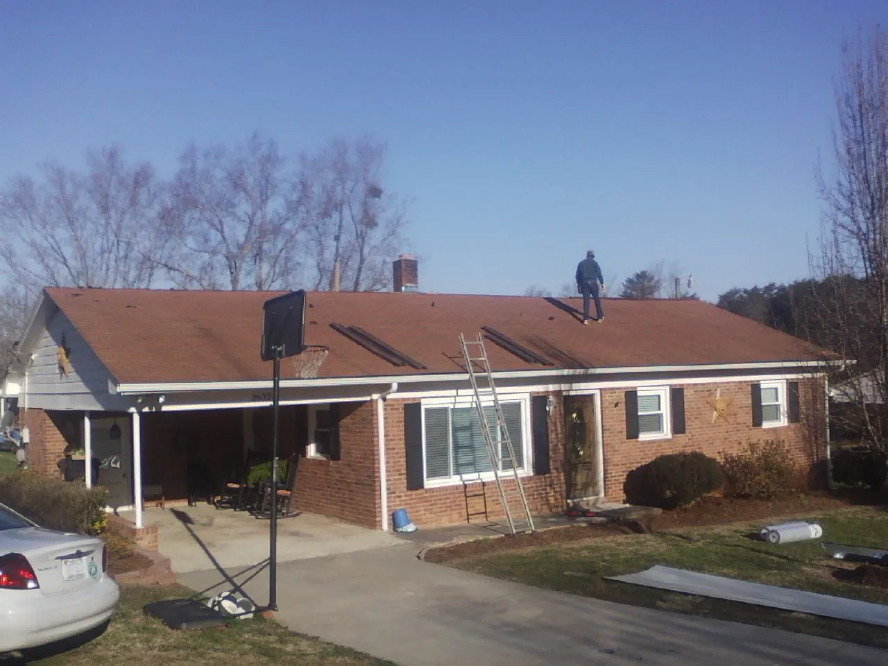 Roofer stripping a shingle roof on a brick ranch before metal panels in Garnett