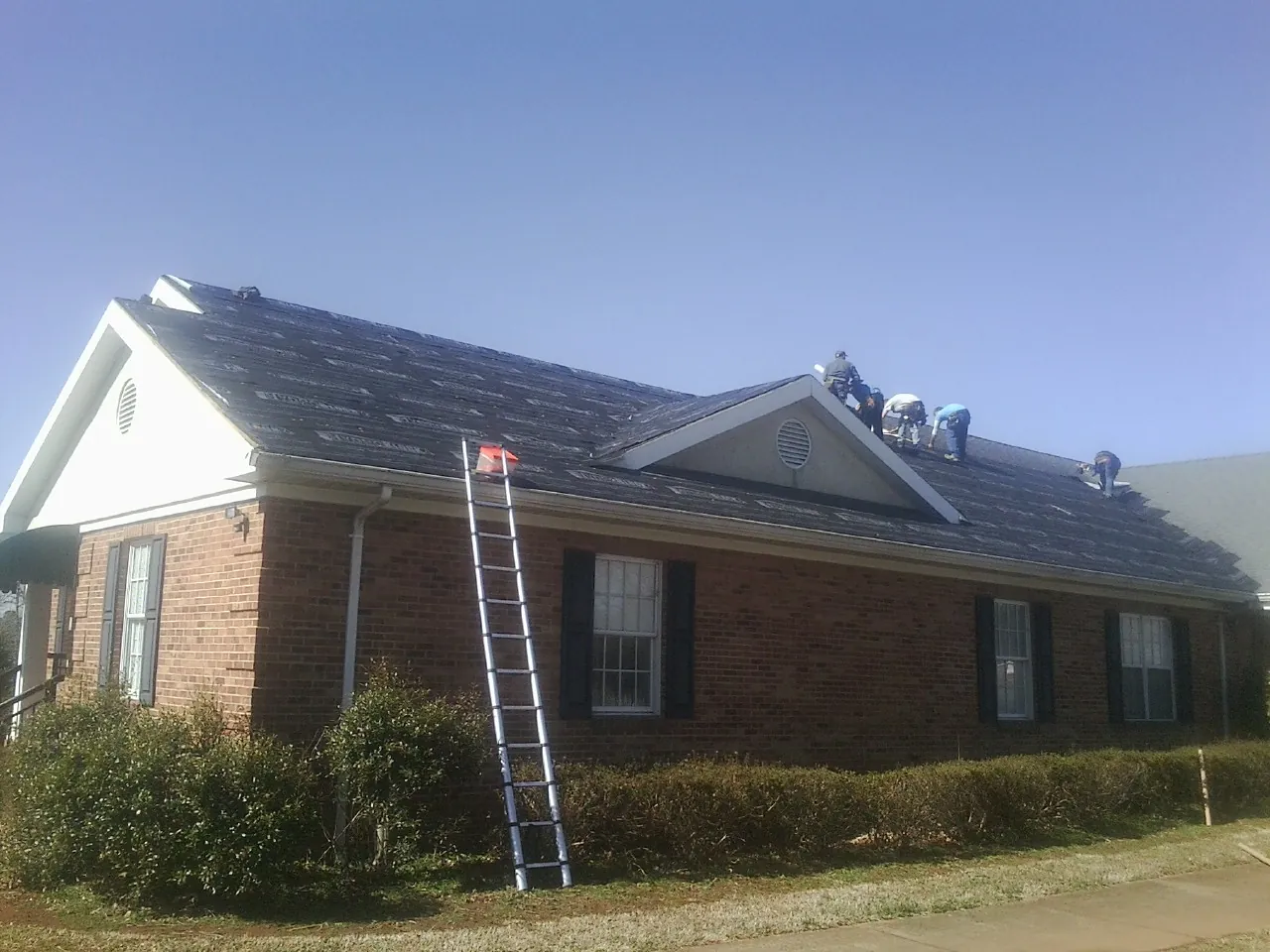 Crew tearing shingles off a brick ranch roof with a ladder set — Emergency Roof Repair work by our crew in Garnett