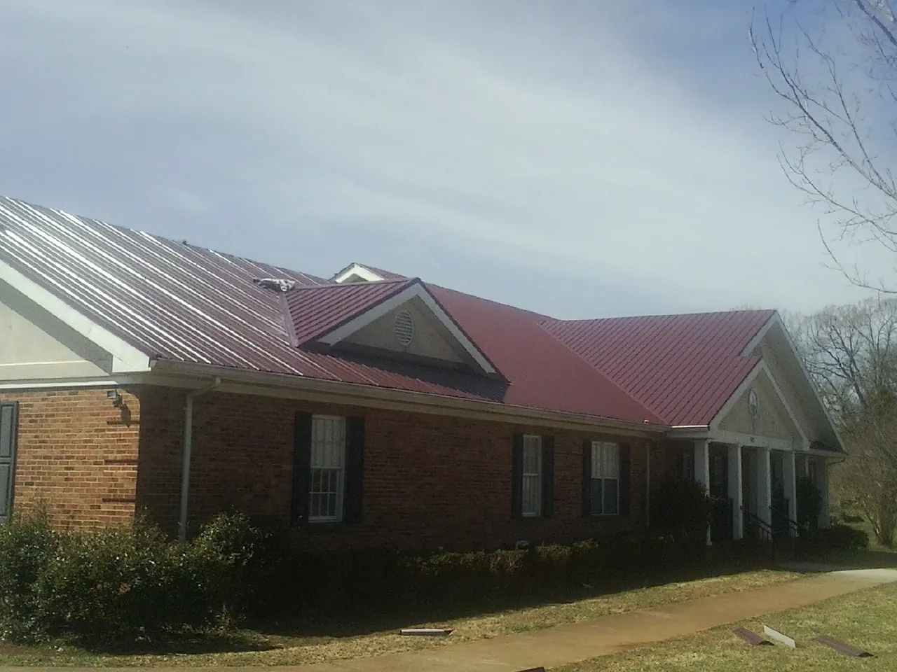 Red metal roof with gabled entries on a long brick building, from a Hail Damage Roof Repair job in Garnett