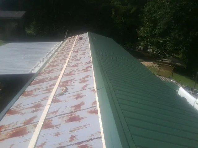 Old rusted panels beside newly installed green metal roofing — Wind Damage Roof Repair by Roofing Brothers in Garnett