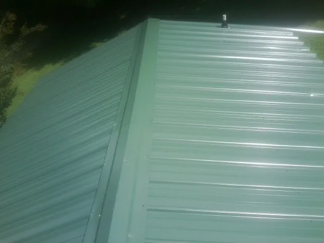 New green metal panels meeting at the ridge of a roof — Flat Roof Repair work by our crew in Garnett