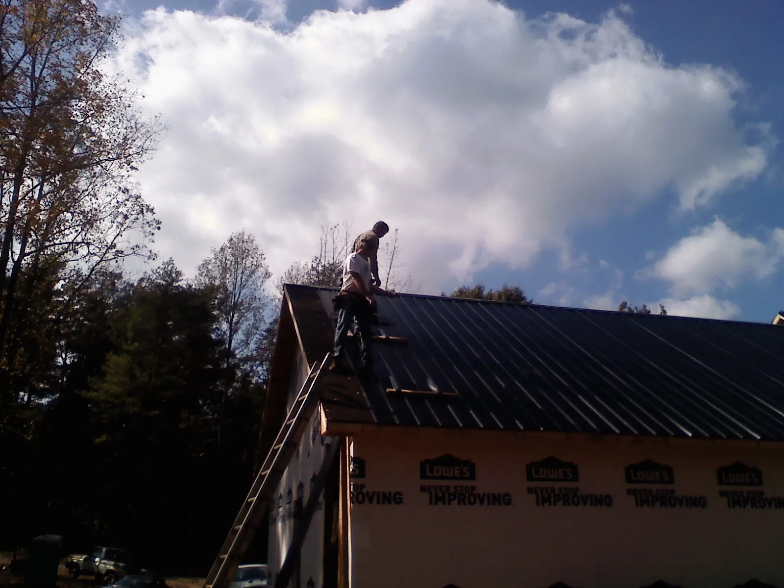 Roofer fastening dark metal panels high against a cloudy sky, from a Roof Inspection job in Garnett