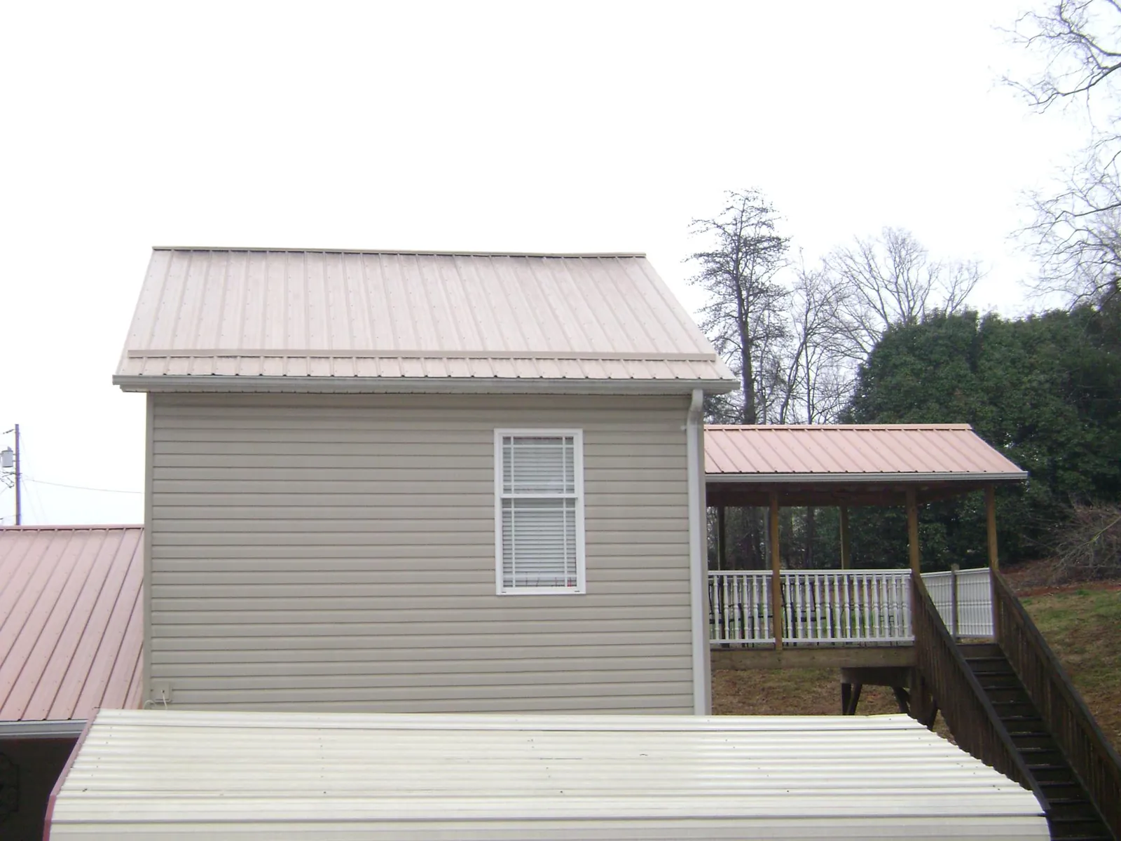 Tan metal roofs on a two story addition and attached porch, from a Roof Replacement job in Garnett